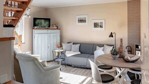 Una sala de estar con sofá, sillas, mesa de comedor, televisor y obras de arte en la pared.