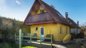 Una casa amarilla con balcón de madera, chimenea y un patio cercado.