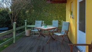 Una terraza de madera con una mesa y sillas, rodeada por una cerca verde y un seto.