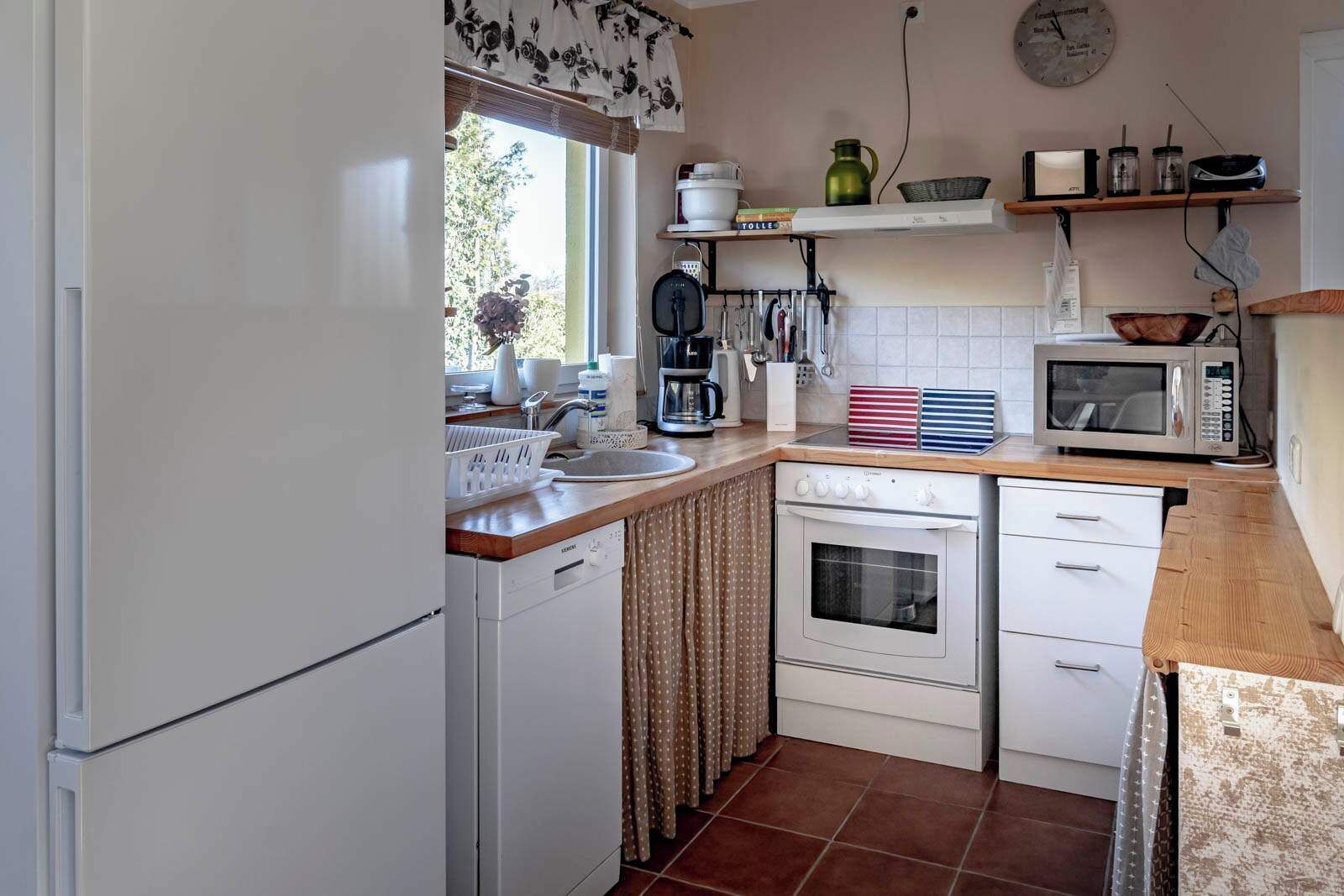 A compact kitchen with a refrigerator, stove, microwave, and a window with curtains.