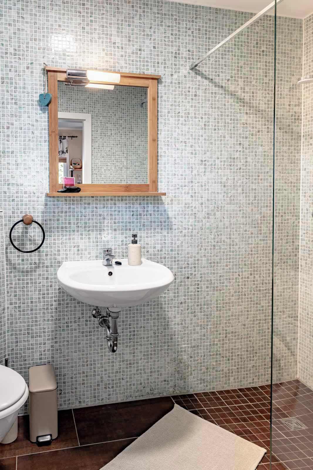 A bathroom with a tiled wall, a sink, a mirror, a toilet, and a shower area.