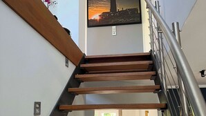 A modern staircase with wooden steps and a metal railing, leading to a landing with a framed picture of a cityscape. - Exklusives Ferienhaus Celeste nahe Warnemünde – Luxus & Entspannung für bis zu 7 Personen (Rostock)