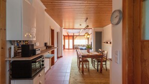 Une cuisine avec un plafond en bois, un coin repas avec une table et des chaises, et une horloge au mur.