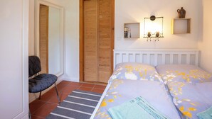 Une chambre à coucher comprenant un lit, une chaise, une armoire en bois et une étagère murale agrémentée d’objets décoratifs.