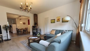 A living room with a sofa, a dining area, a fireplace, and a chandelier. - Ferienhaus Neuland 5 - Entspannung in Seenähe (Lychen)
