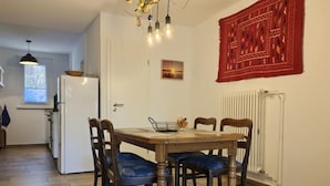 A dining area with a wooden table, four chairs, a chandelier, and a red patterned wall hanging. - Ferienhaus Neuland 5 - Entspannung in Seenähe (Lychen)