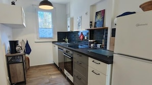 A modern kitchen with a black countertop, stainless steel appliances, and a window with blinds. - Ferienhaus Neuland 5 - Entspannung in Seenähe (Lychen)