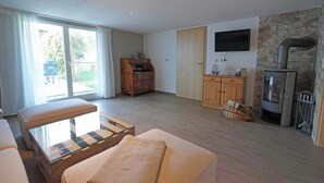 Un salon comprenant un canapé, une table basse en verre, un meuble en bois, un mur en pierre, une cheminée et un téléviseur fixé au mur.