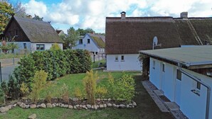 Un quartier résidentiel où les maisons se distinguent par leurs toits de chaume et leurs murs blancs, et où elles sont entourées d’un jardin bien entretenu, agrémenté de diverses plantes et bordé de pierres.