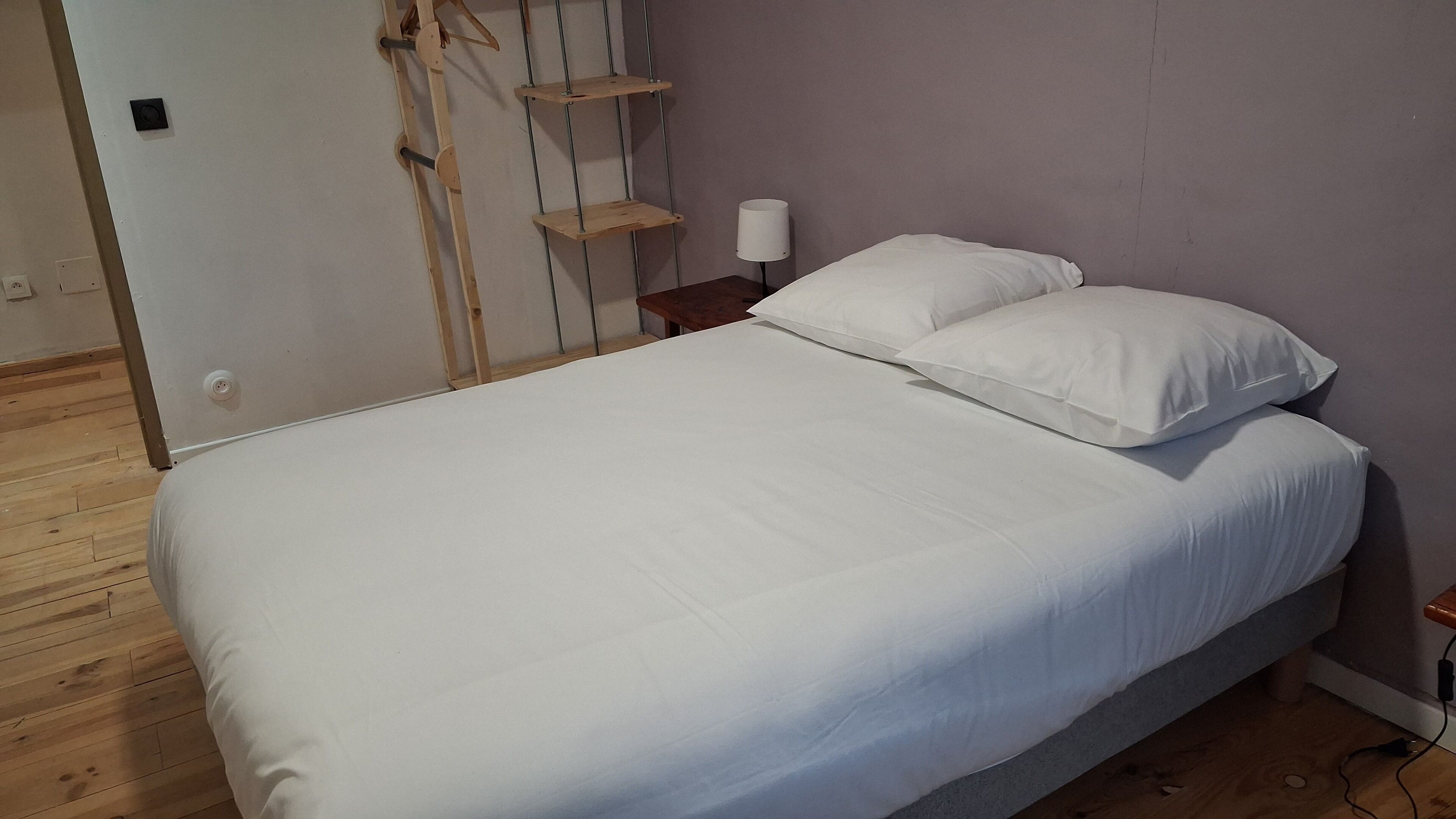 Ein Schlafzimmer mit Holzboden, einem Bett mit weißer Bettwäsche, einem Nachttisch mit Lampe und einer Holzleiter an der Wand.
