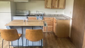 A compact kitchen with wooden cabinets, a built-in stove, and a small island with chairs.