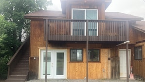 A two-story wooden house with a balcony, a front door, and a staircase leading to the upper level.