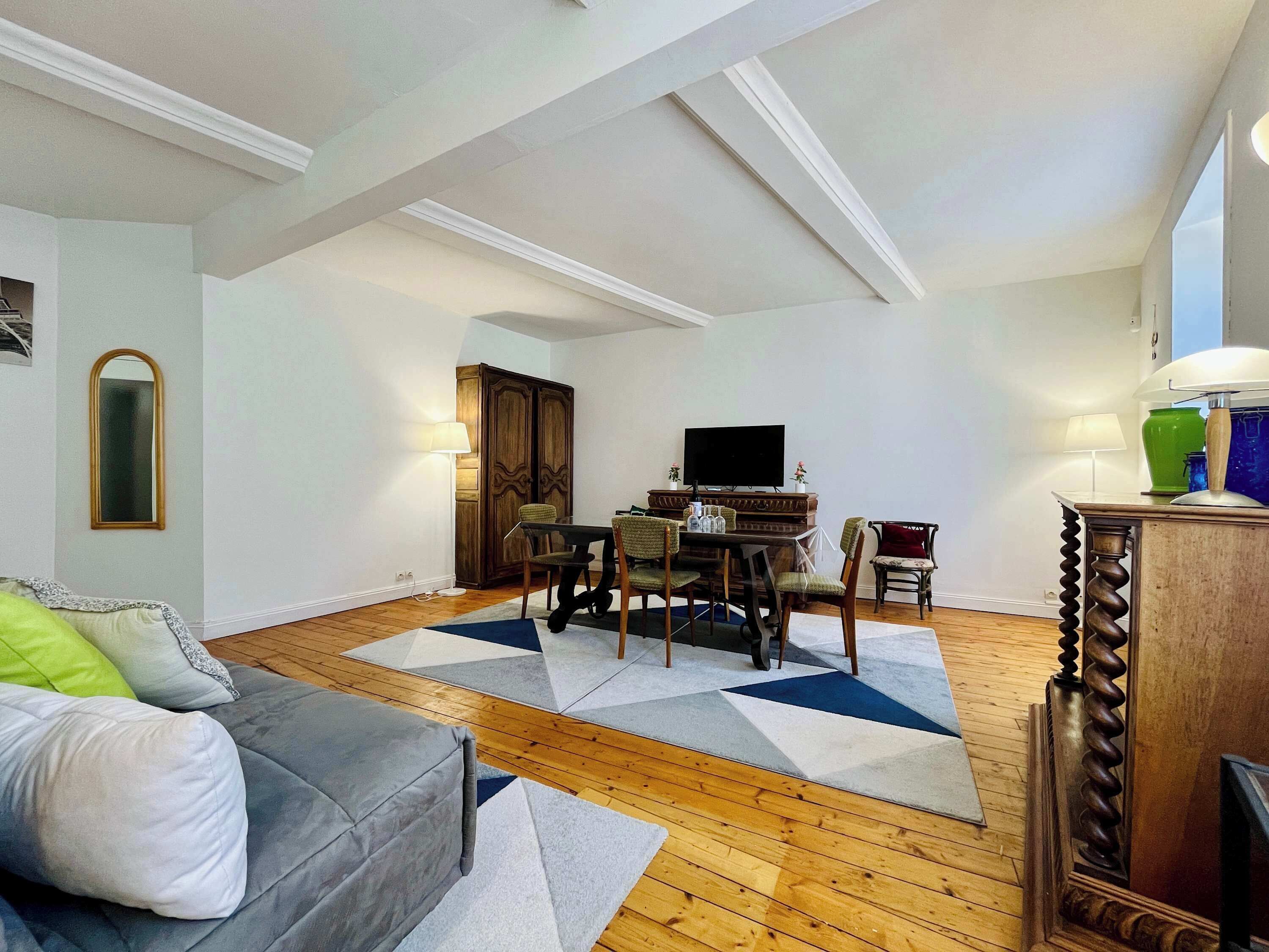 Een woonkamer met een bank, een eettafel met stoelen, een televisie en een houten kast.