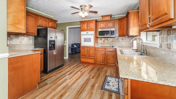 A kitchen with wooden cabinets, a stainless steel refrigerator, an oven, a microwave, and a ceiling fan. - Peaceful almost 4 acres  pond,sunroom, close to shopping restaurant's Douglas,GA (Douglas)
