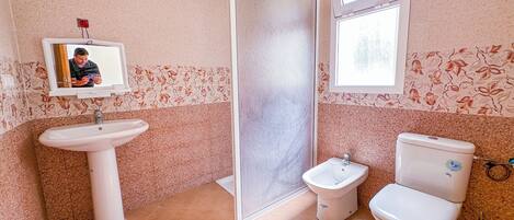 A bathroom with a sink, toilet, bidet, and a shower area.