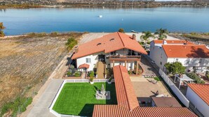 Una casa grande con techo de tejas rojas, piscina y vista a un lago.