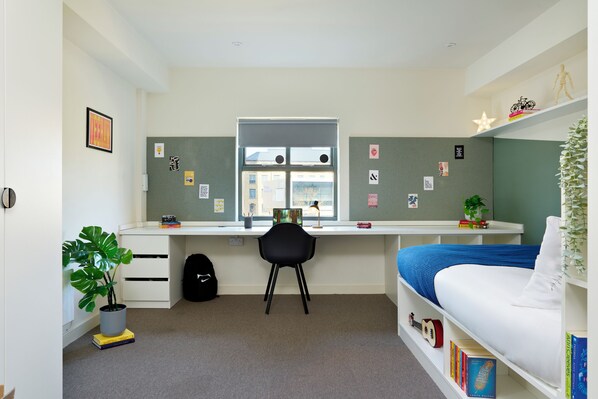 Une pièce comprenant un bureau, une chaise, un lit et des étagères remplies de livres et d’objets décoratifs.