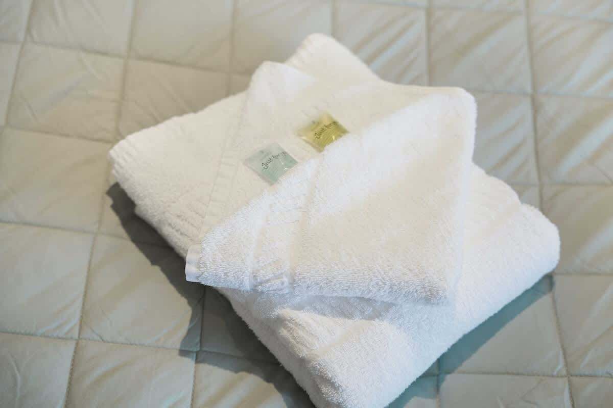 Une serviette blanche, soigneusement pliée, est posée sur un lit recouvert d’une courtepointe.