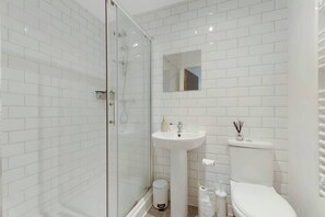 Ein modernes Badezimmer mit weißen Fliesen, einer Duschkabine, einem Standwaschbecken und einer Toilette.