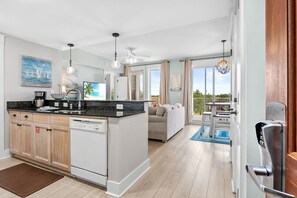 A modern kitchen with a central island, white cabinetry, and a dining area with a view. - Stylish 2BR/2BA Resort Condo In Baytowne Wharf (Miramar Beach)