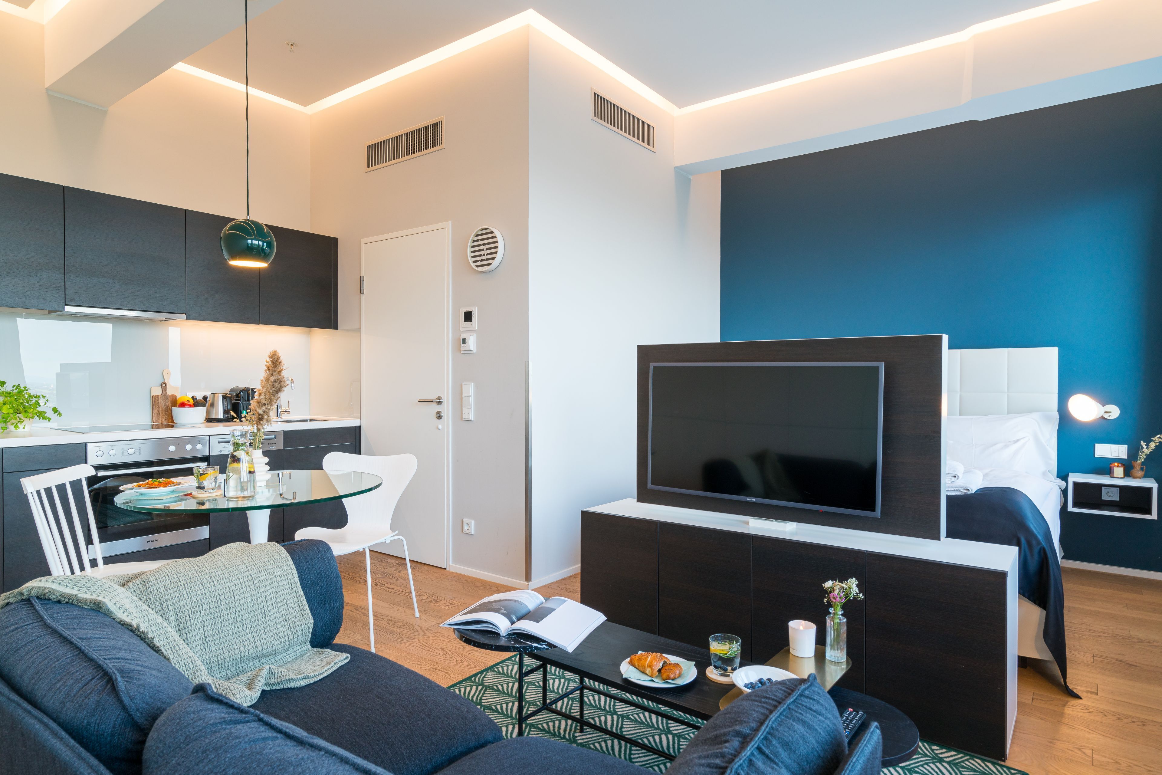 Ein modernes Wohnzimmer mit Flachbildfernseher, einer Couch, einem Couchtisch und einem Essbereich mit Tisch und Stühlen.