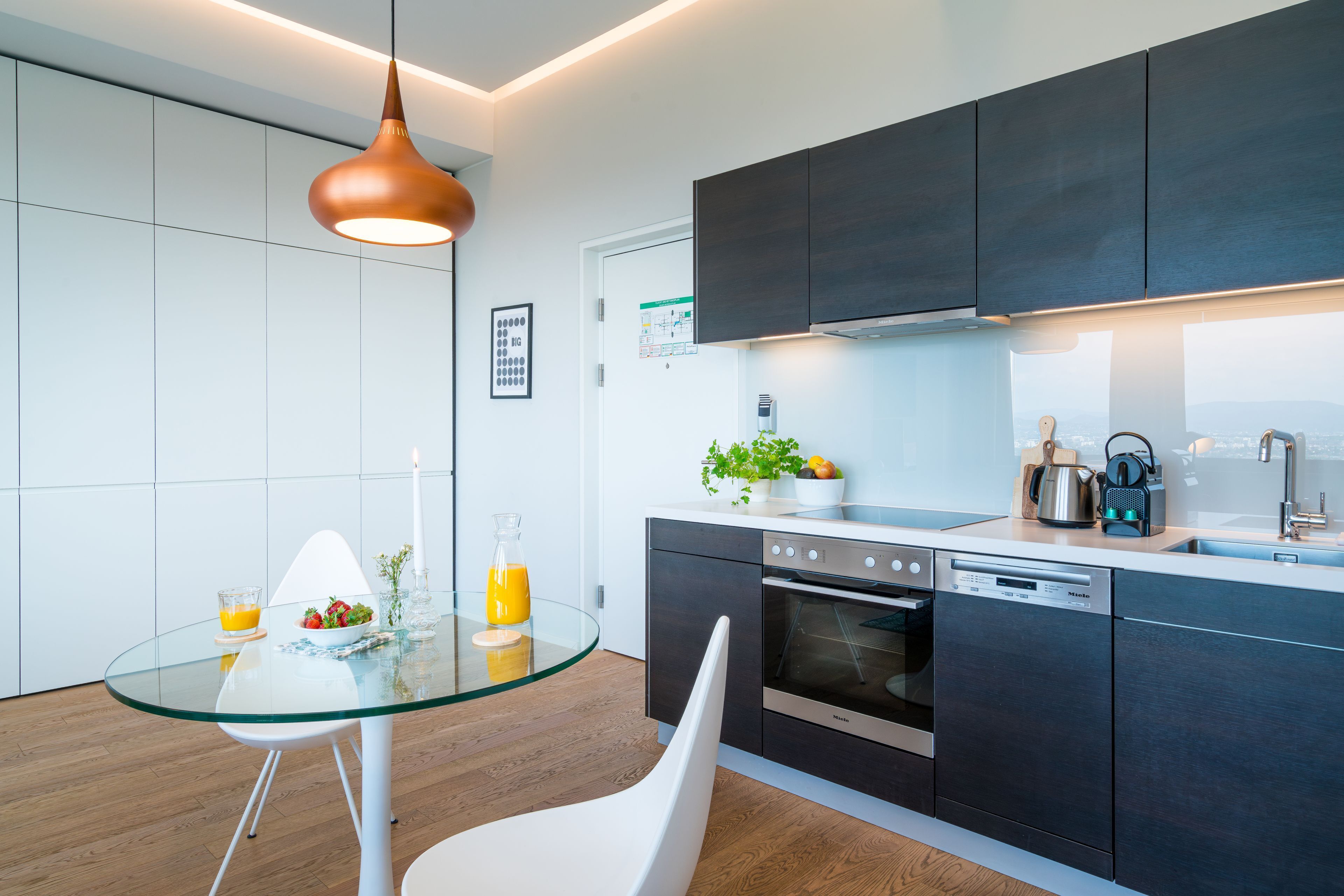 A modern kitchen with dark cabinets, a glass dining table, and a hanging pendant light.