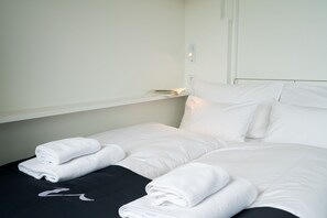 A neatly made bed with white linens and towels, a bedside table with a book, and a wall-mounted light. - Vienna Residence, Philips Haus - Euro Plaza #6573 (Vienna)