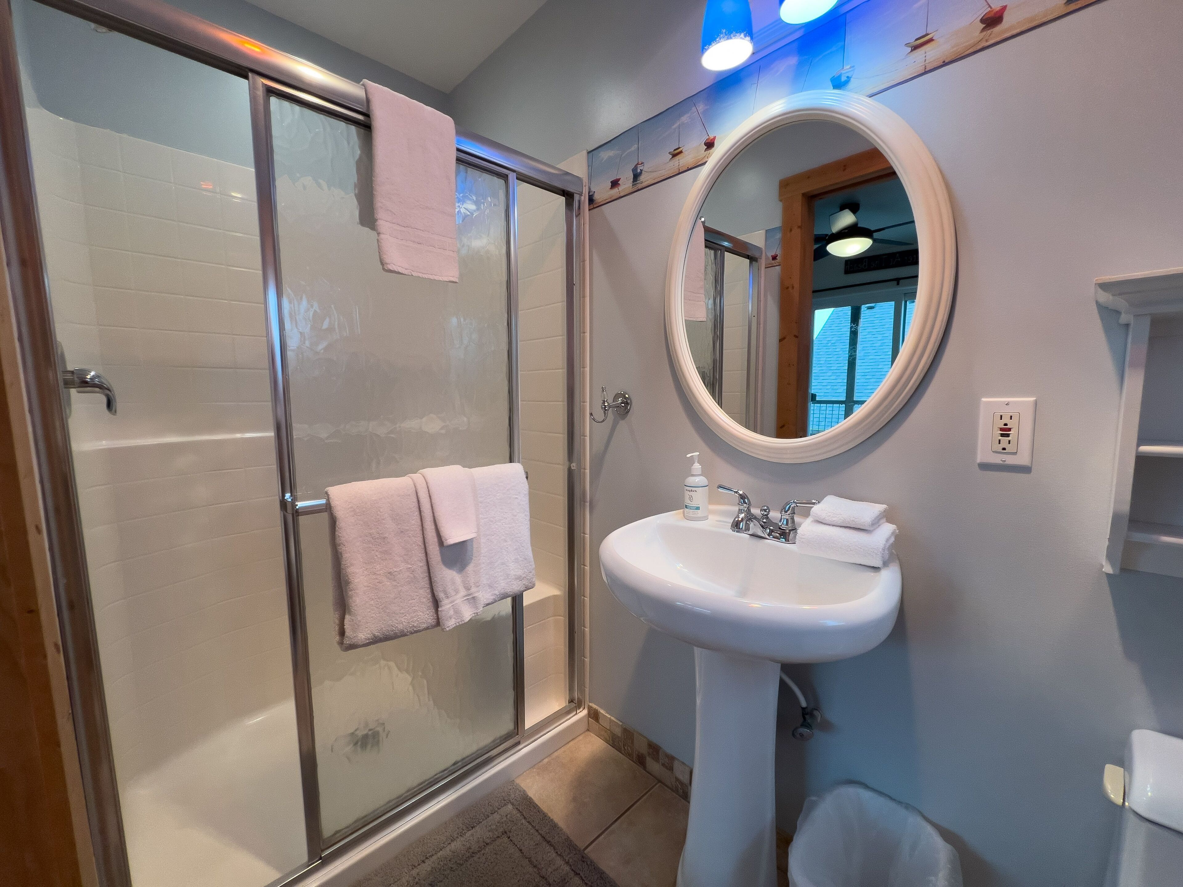 Een badkamer met een douchecabine van glas, een wastafel op een voetstuk en een ronde spiegel.