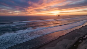 A beach with waves, a sunset, and a distant island.