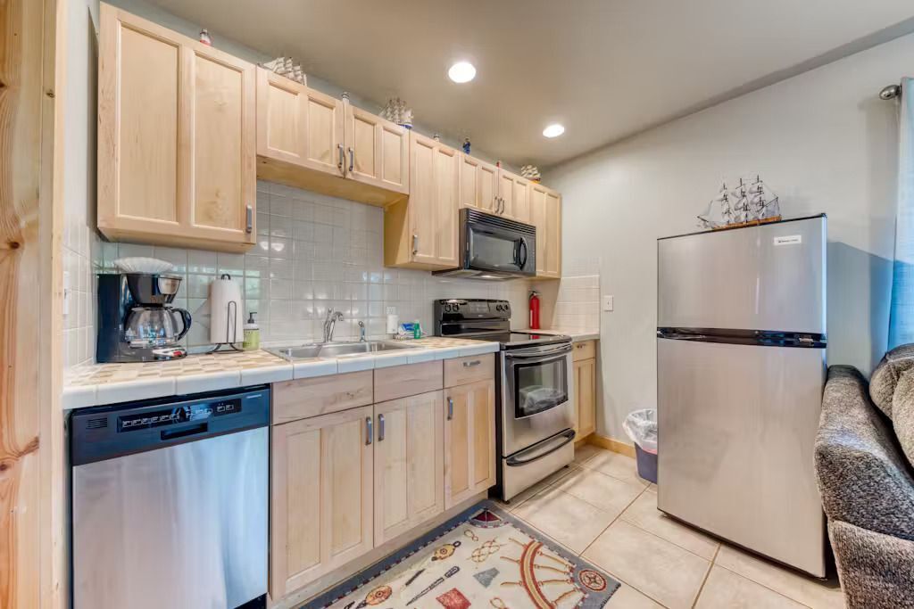 A compact kitchen with wooden cabinets, a stainless steel refrigerator, a microwave, an oven, and a dishwasher.