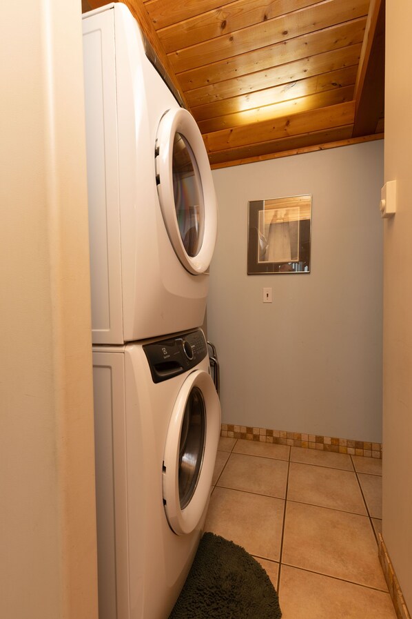 A laundry area with stacked washing machines, a mirror, and a tiled floor.