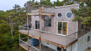 A multi-level wooden house with a balcony, large windows, and a staircase.