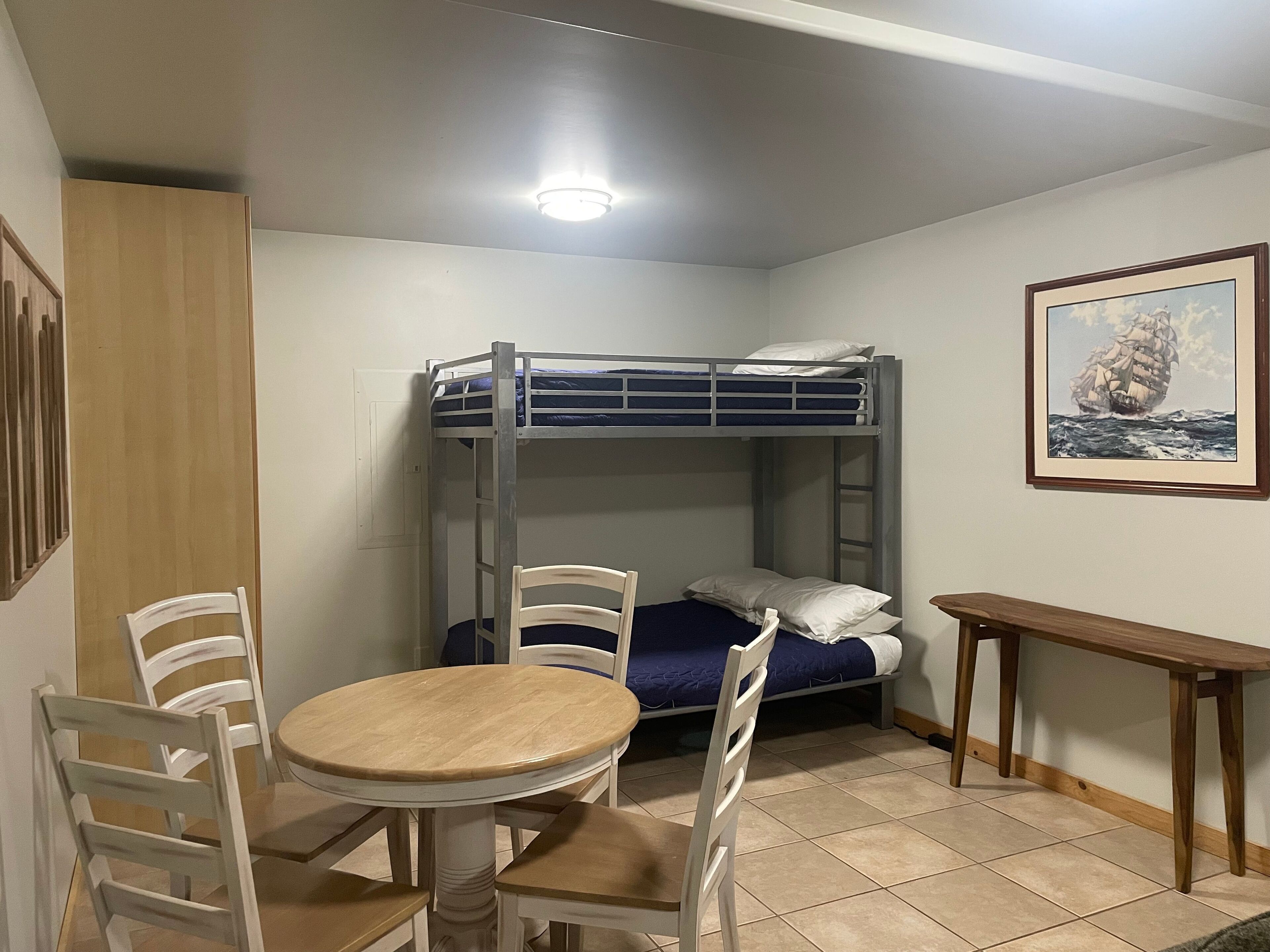 A bunk bed with a headboard, a round wooden table with chairs, and a framed picture on the wall.