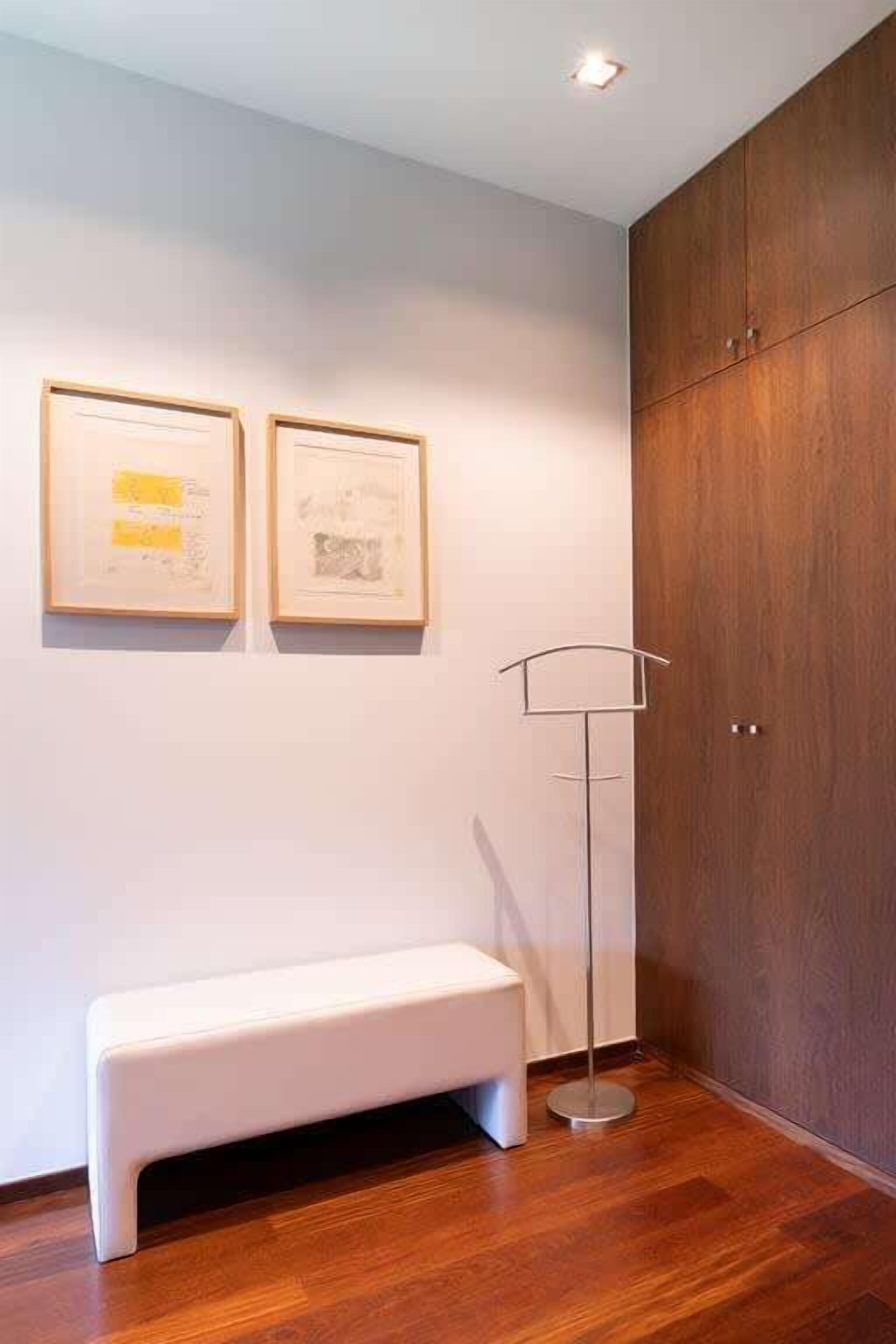Een kamer met een witte bank, houten vloeren, een hoge vloerlamp en twee kunstwerken in lijsten aan de muur.