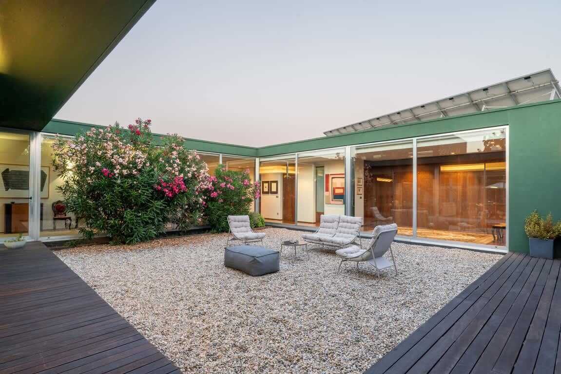 An outdoor patio with seating, a large window, and a garden with pink flowers.