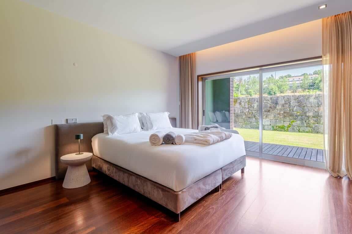 Un dormitorio moderno con una cama grande, una mesita de noche y vistas a un muro de piedra y vegetación.