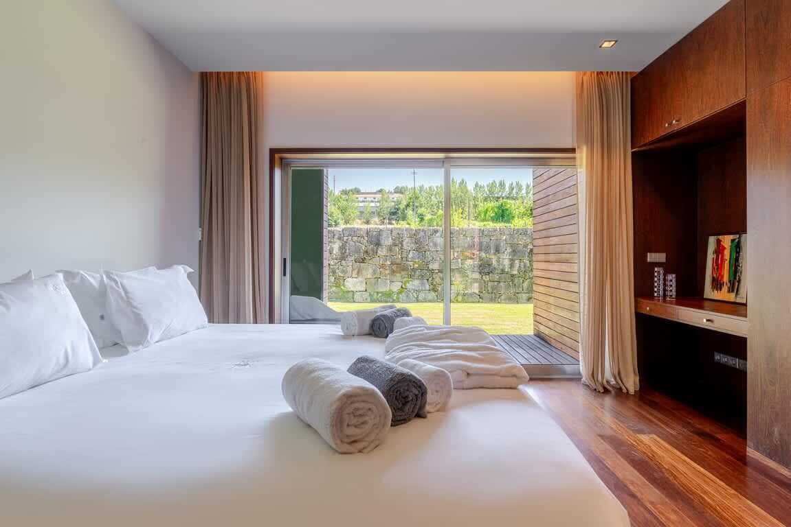 A hotel room with a large bed, a wooden floor, a sliding glass door to an outdoor area, and a built-in wooden cabinet.