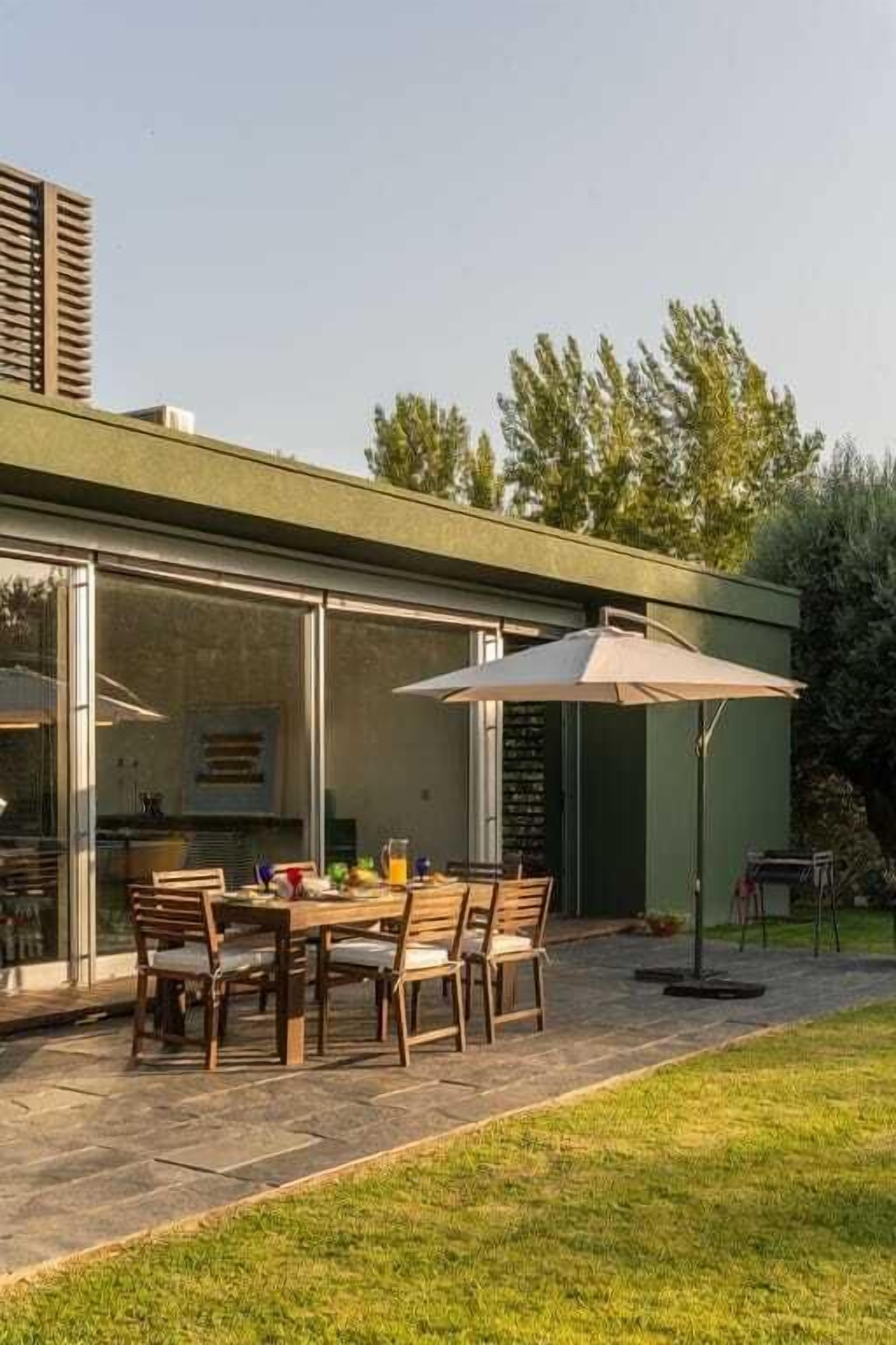 Eine moderne Außenpatio mit Esstisch und Stühlen, einem großen Sonnenschirm und einem gepflasterten Weg.