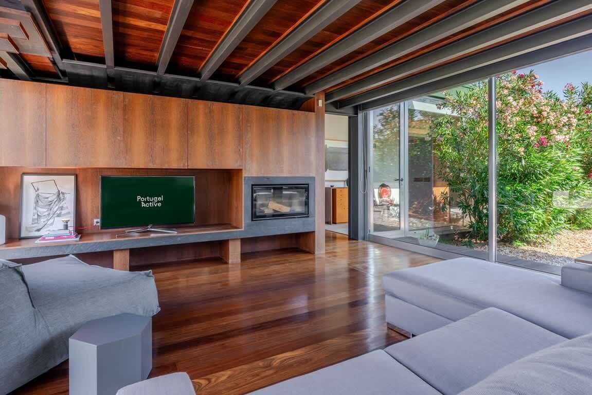 A modern living room with a fireplace, a television, and a large window overlooking greenery.
