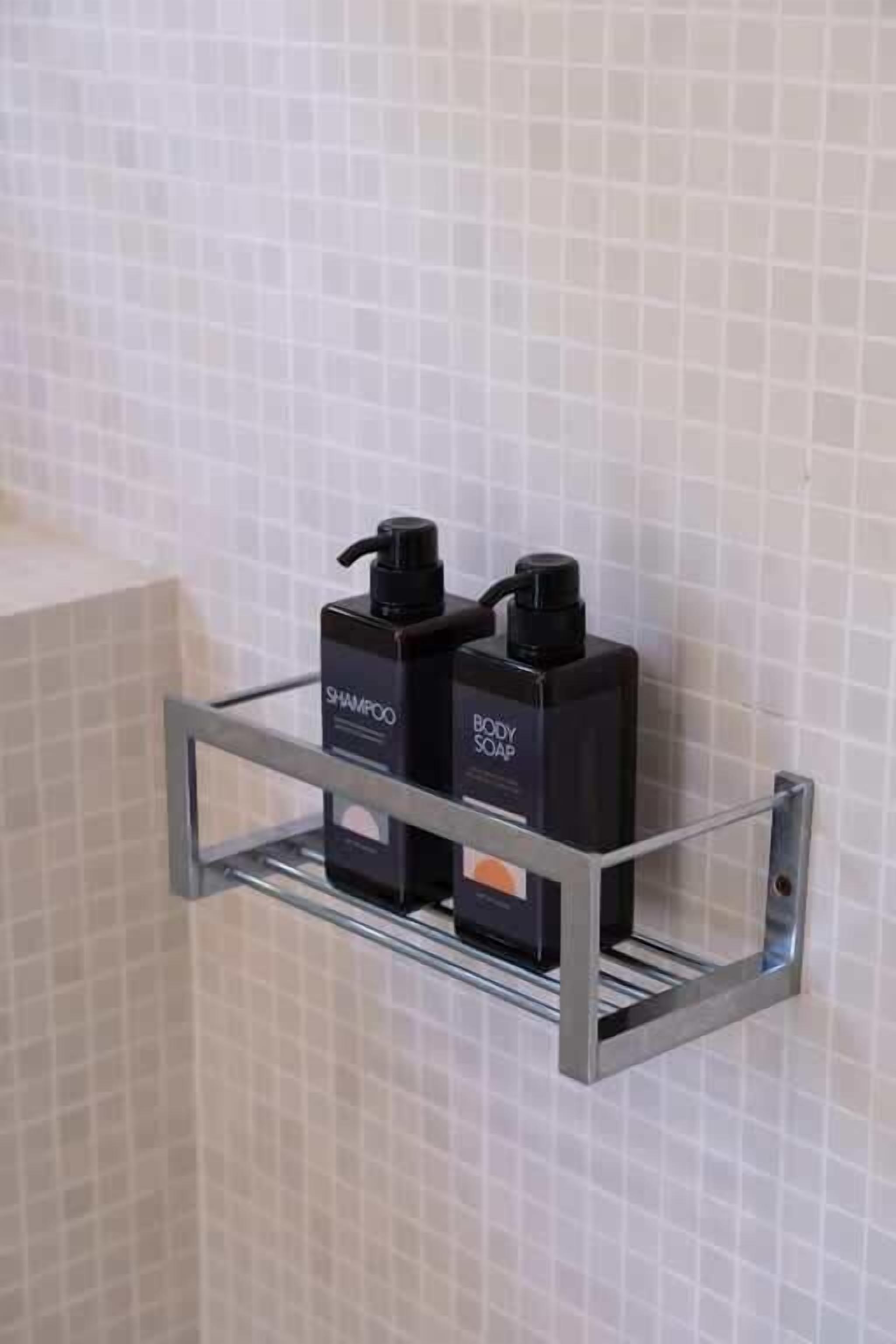 A bathroom with a tiled wall and a metal shelf holding two bottles of shampoo and body soap.