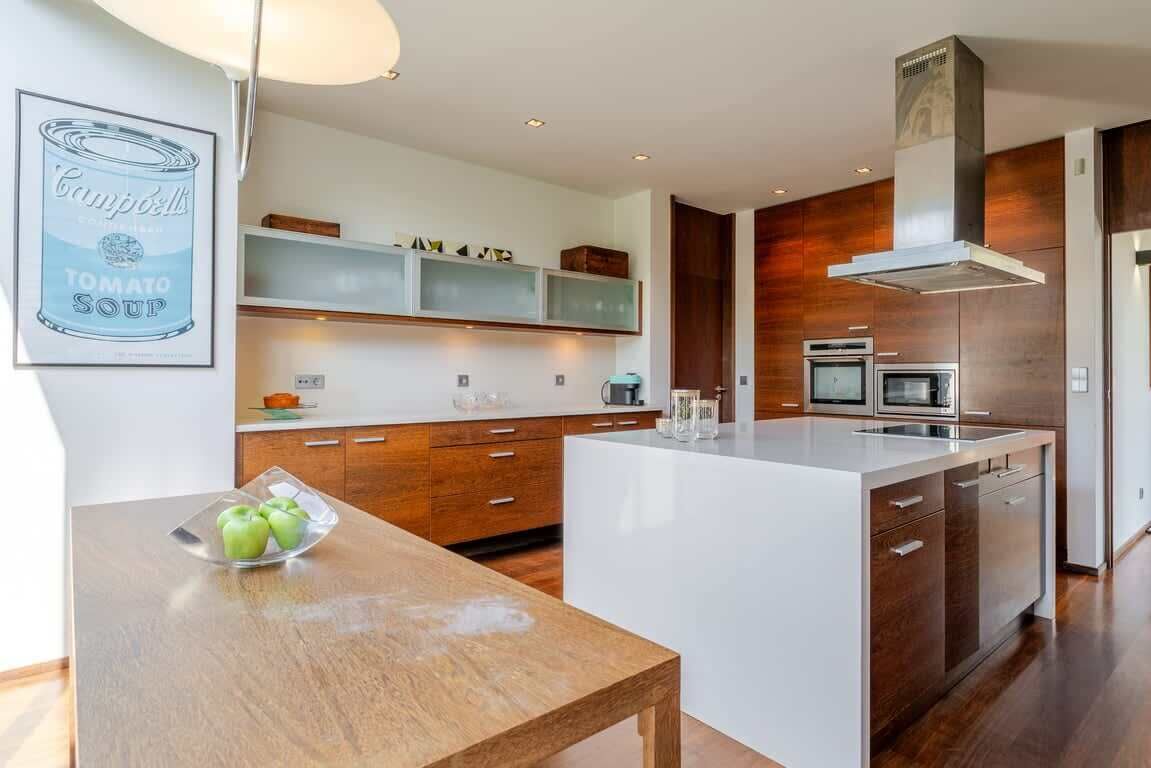 A modern kitchen with a central island, wooden cabinets, and a built-in oven.