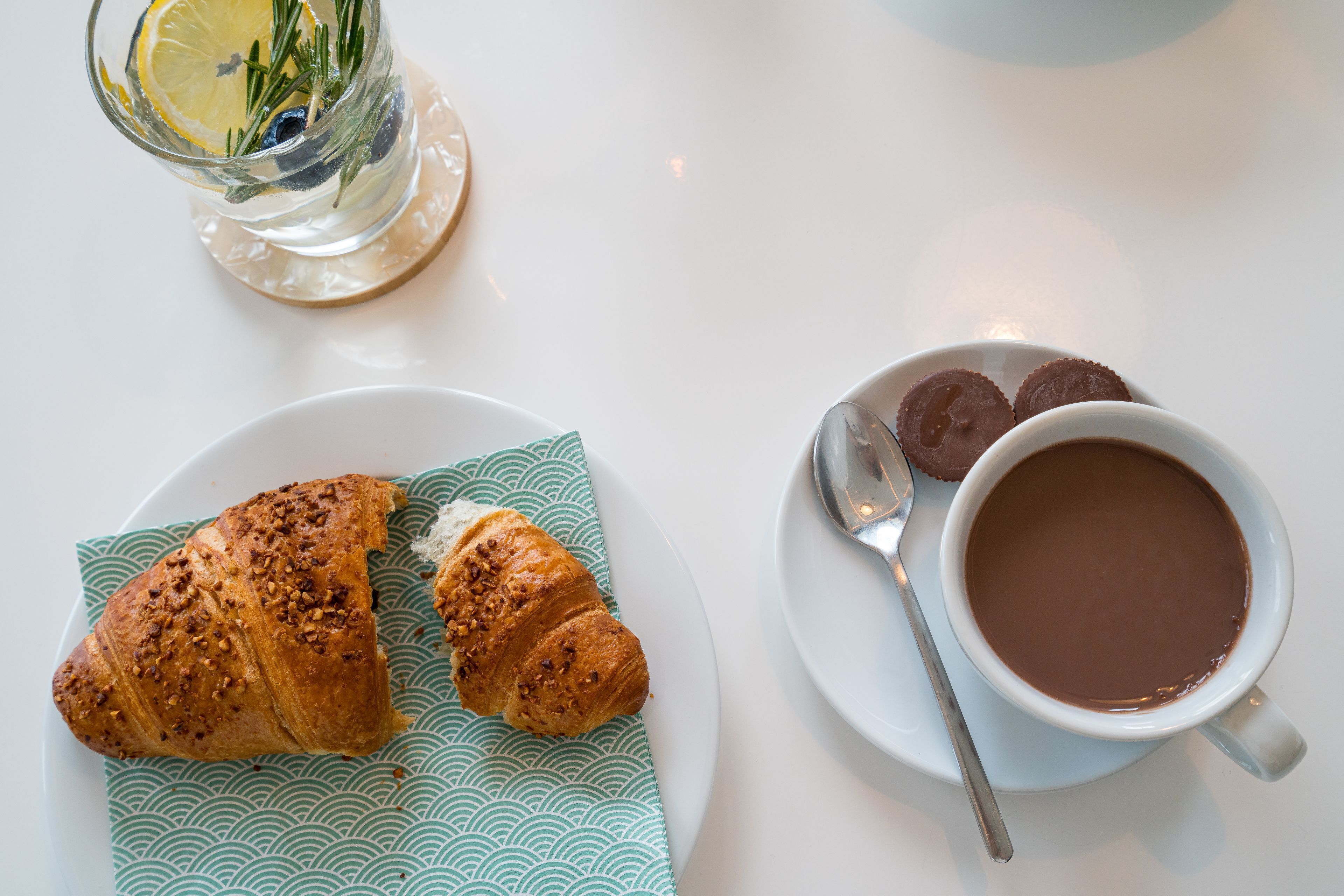 Een bord met croissants en een kop hete chocolademelk op een witte tafel.