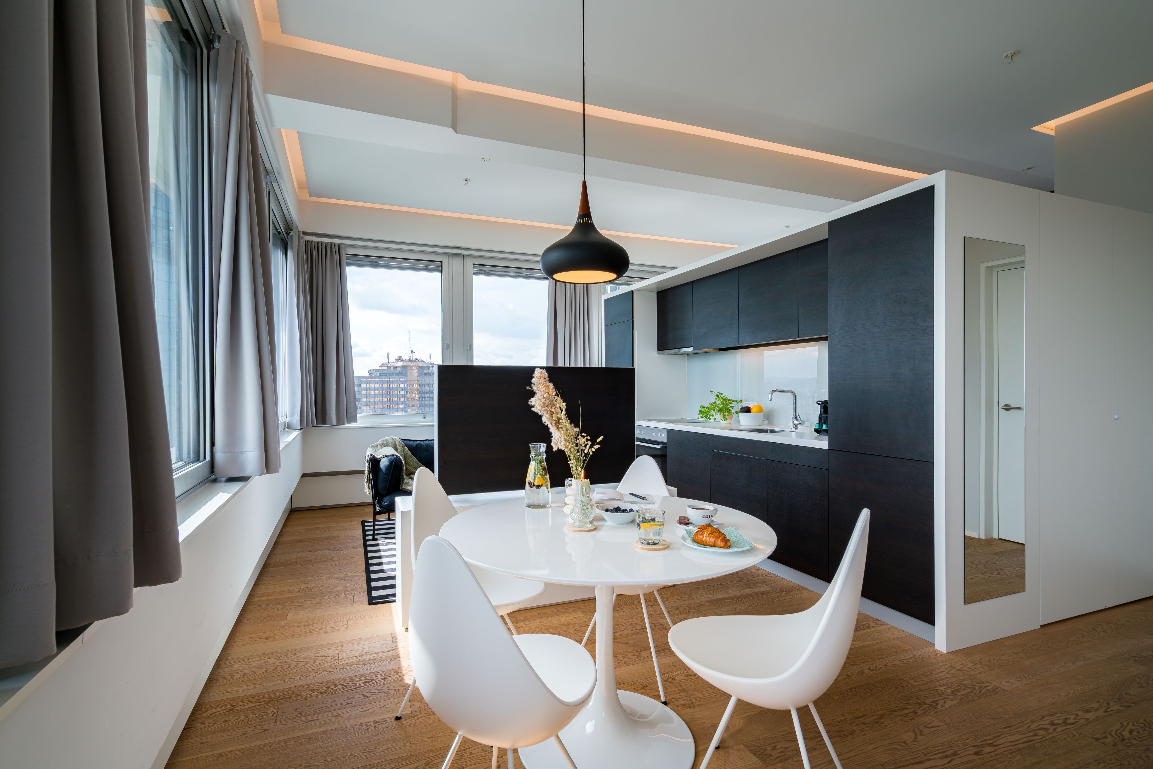 A modern dining area with a round white table, white chairs, and a pendant light.