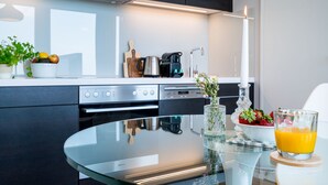 A modern kitchen with a glass table, a coffee maker, a bowl of fruit, and a candle. - Vienna Residence, Philips Haus - Euro Plaza #6526 (Vienna)