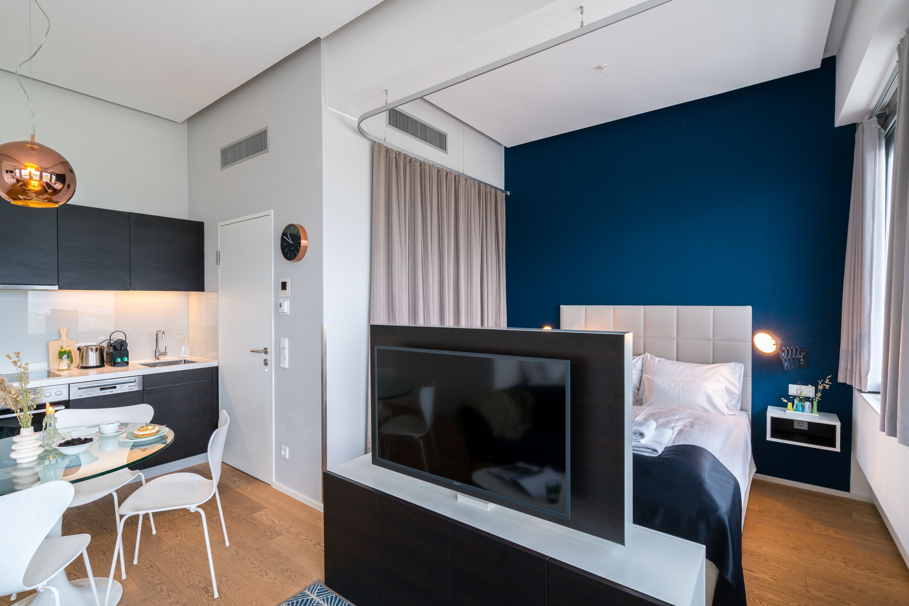 Een moderne hotelkamer met een flatscreen televisie, een bed met witte lakens, een klein nachtkastje en een blauw accentmuur.