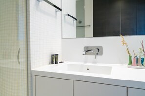 A bathroom with a white sink, a mirror, and a shower area.