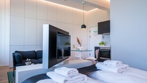 Camera d'albergo moderna con un letto, un divano, una TV, un tavolino con un vaso e angolo cottura.
