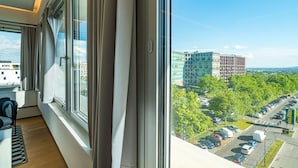 A modern hotel room with large windows, a view of a parking lot, and a cityscape in the background. - Vienna Residence, Philips Haus - Euro Plaza #6554 (Vienna)