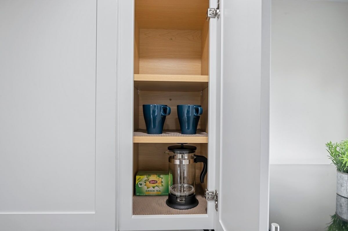 A kitchen cabinet with a coffee maker, two blue mugs, and a box of Lipton green tea.