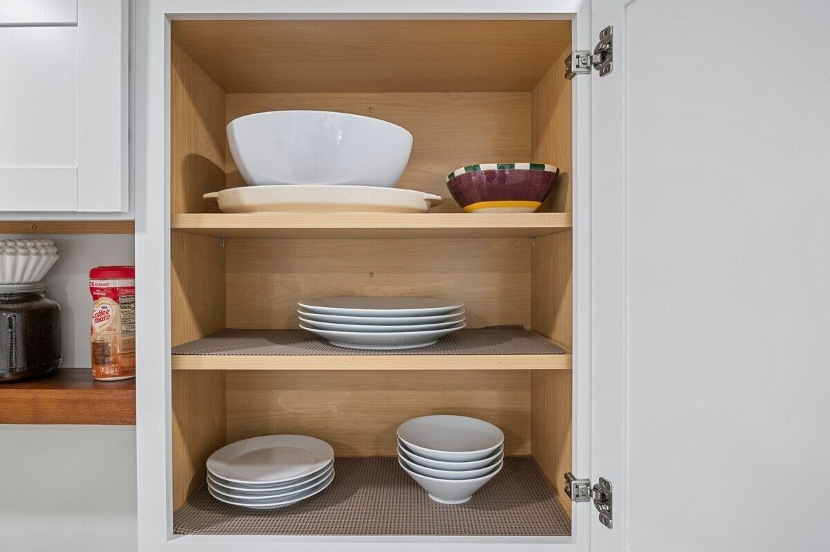 A kitchen cabinet with three shelves, each holding bowls and plates.